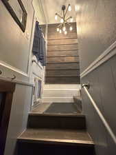 Staircase with a decorative wall, a chandelier, and a wainscoted wall