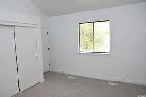 Unfurnished bedroom featuring carpet floors, a closet, and lofted ceiling