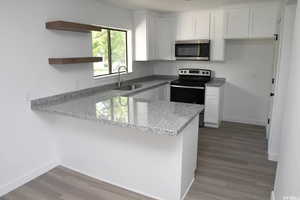 Kitchen with a peninsula, open shelves, stainless steel appliances, light stone countertops, and white cabinets