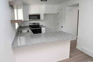 Kitchen featuring stainless steel appliances, light stone countertops, a peninsula, white cabinets, and light wood-style floors