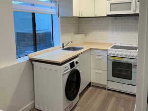 Kitchen with light countertops, white appliances, washer / dryer, a textured ceiling, and wood finished floors