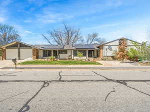 Mid-century modern home with an attached garage, brick siding, roof mounted solar panels, and driveway