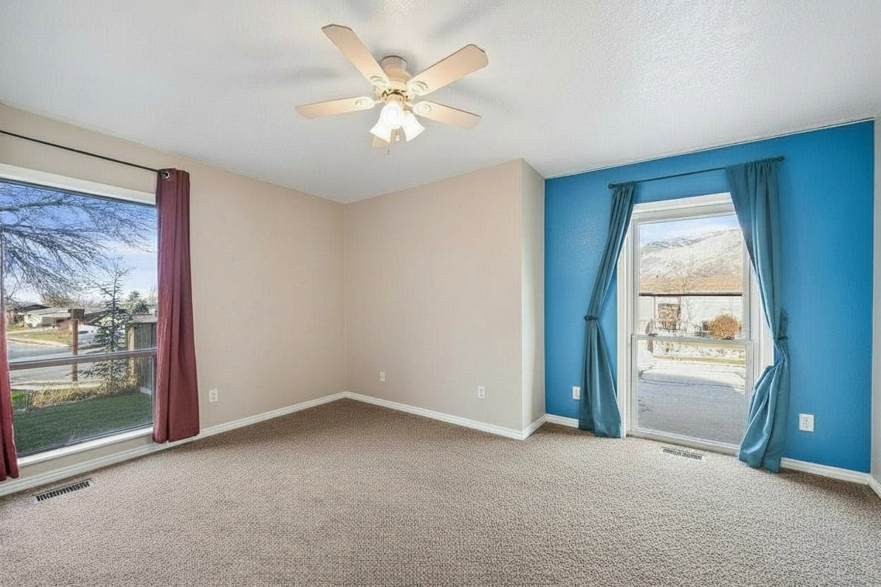Spacious room featuring carpeted flooring, a ceiling fan with integrated lighting, and a large window with street views