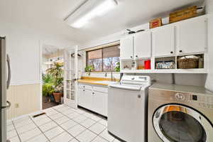 Laundry room with wainscoting, washing machine and clothes dryer, cabinet space, and light tile patterned flooring