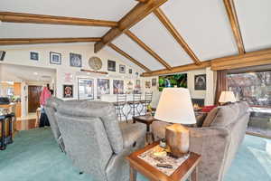 Living area with carpet flooring, plenty of natural light, a lit fireplace, beam ceiling, and high vaulted ceiling