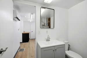 Half bath with vanity, a wall unit AC, and light wood-type flooring