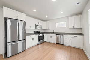 Kitchen featuring appliances with stainless steel finishes, white cabinetry, light wood-style flooring, recessed lighting, and dark countertops