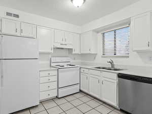 Kitchen with white appliances, white cabinetry, light tile patterned floors, light countertops, and a textured ceiling