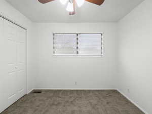 Bedroom with a closet, dark carpet, and a ceiling fan