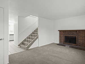 Living room featuring light colored carpet, a brick fireplace, light tile patterned floors, and stairway