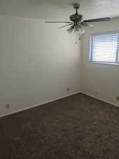Spare room with dark colored carpet, a textured ceiling, and a ceiling fan