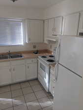 Kitchen with white appliances, white cabinetry, light tile patterned floors, and under cabinet range hood