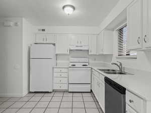 Kitchen featuring white appliances, a textured ceiling, white cabinetry, light tile patterned floors, and under cabinet range hood