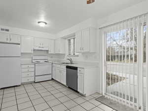 Kitchen featuring white appliances, white cabinets, a textured ceiling, light countertops, and light tile patterned floors