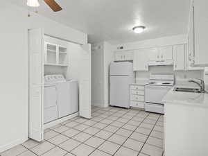 Kitchen with white appliances, light tile patterned floors, white cabinetry, a textured ceiling, and washer and clothes dryer