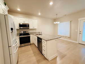 Kitchen featuring stainless steel appliances, light stone countertops, a peninsula, white cabinets, and pendant lighting