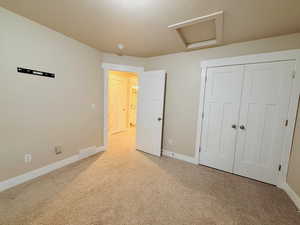 Unfurnished bedroom featuring attic access, light carpet, a closet, and a textured ceiling