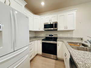 Kitchen featuring stainless steel appliances, white cabinetry, light wood-style flooring, and light stone counters
