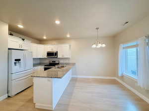 Kitchen with appliances with stainless steel finishes, white cabinetry, dark stone counters, hanging light fixtures, and light wood-type flooring