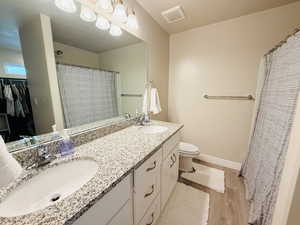 Full bath with double vanity, a shower with shower curtain, light wood-style floors, and a spacious closet