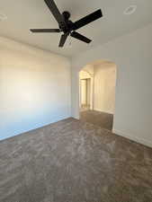 Den/office with arched walkways, carpet, and a ceiling fan