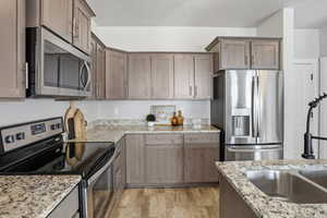 Kitchen featuring appliances with stainless steel finishes, light stone counters, and light wood-type flooring