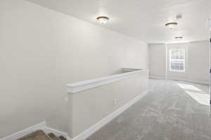 Hall with carpet floors, an upstairs landing, and a textured ceiling