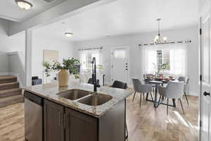 Kitchen featuring open floor plan, a kitchen island with sink, light stone countertops, dark brown cabinets, and stainless steel dishwasher