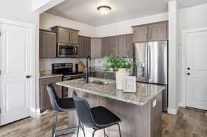 Kitchen with light stone counters, appliances with stainless steel finishes, an island with sink, a breakfast bar area, and dark brown cabinetry