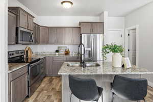 Kitchen featuring appliances with stainless steel finishes, light stone counters, light wood finished floors, and a center island with sink