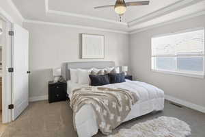 Carpeted bedroom featuring crown molding, a tray ceiling, and ceiling fan