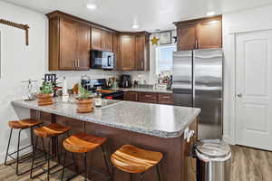 Kitchen featuring a peninsula, freestanding refrigerator, a breakfast bar area, light wood finished floors, and recessed lighting