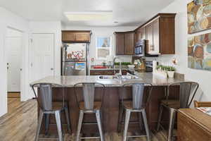 Kitchen featuring dark brown cabinetry, a breakfast bar, appliances with stainless steel finishes, wood finished floors, and a peninsula