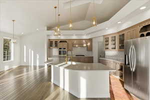 Kitchen with glass insert cabinets, stainless steel fridge with ice dispenser, vaulted ceiling, light countertops, and hanging light fixtures