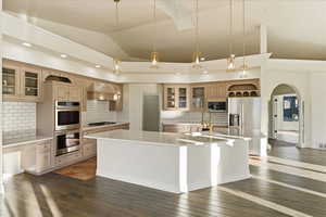Kitchen featuring glass insert cabinets, arched walkways, ornamental molding, appliances with stainless steel finishes, and custom range hood