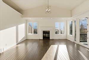 Unfurnished living room with plenty of natural light, a fireplace, a chandelier, dark wood-type flooring, and crown molding