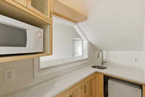 Kitchen featuring vaulted ceiling, white microwave, light stone countertops, dishwasher, and glass insert cabinets