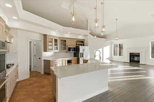 Kitchen with pendant lighting, glass insert cabinets, appliances with stainless steel finishes, a kitchen island with sink, and open floor plan