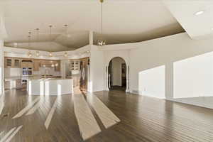 Unfurnished living room with arched walkways, dark wood finished floors, high vaulted ceiling, and recessed lighting