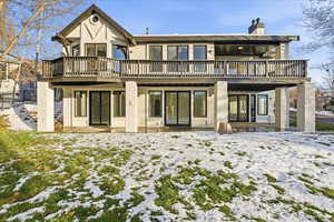 Snow covered back of property featuring a patio area, stucco siding, and a chimney