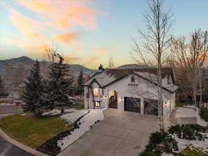 View of front of house with stucco siding, a chimney, driveway, an attached garage, and a front lawn