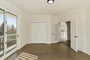 Unfurnished bedroom featuring arched walkways, access to outside, crown molding, dark wood-type flooring, and french doors