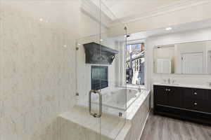 Full bathroom with double vanity, ornamental molding, a shower stall, a bath, and light wood-style floors