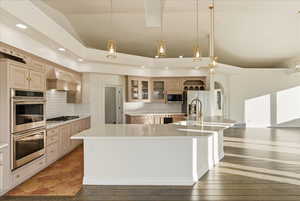Kitchen featuring hanging light fixtures, appliances with stainless steel finishes, glass insert cabinets, a spacious island, and ornamental molding