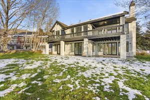 Snow covered property featuring a patio, a chimney, stucco siding, and a balcony