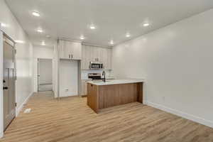 Kitchen featuring a peninsula, modern cabinets, appliances with stainless steel finishes, light wood finished floors, and light stone countertops
