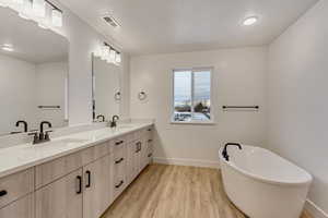 Full bath with a freestanding bath, double vanity, and light wood-type flooring