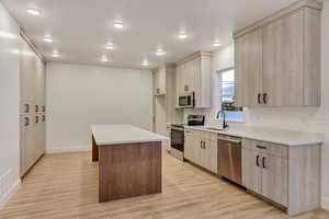 Kitchen with a kitchen island, light brown cabinetry, appliances with stainless steel finishes, light wood-type flooring, and recessed lighting