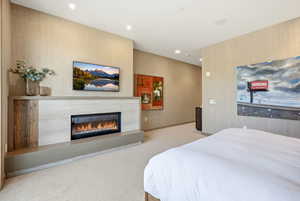 Bedroom featuring wallpapered walls, light colored carpet, recessed lighting, and a glass covered fireplace