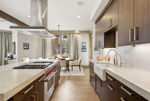 Kitchen with dark brown cabinets, designer stove, light stone countertops, island range hood, and recessed lighting